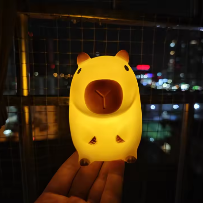 Yellow capybara-shaped night light held in front of a cityscape at night.